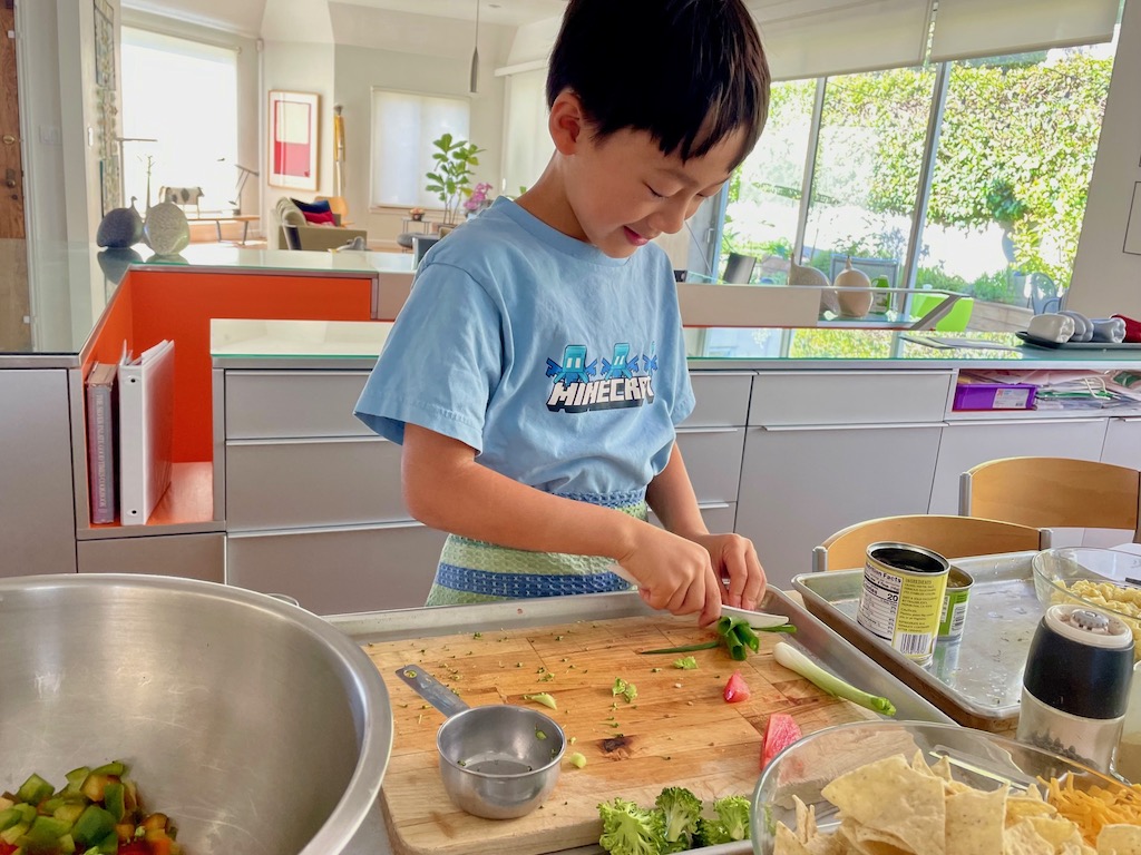 The safest way to cut is to use a plastic knife. Chid slices green onions with the plastic knife.