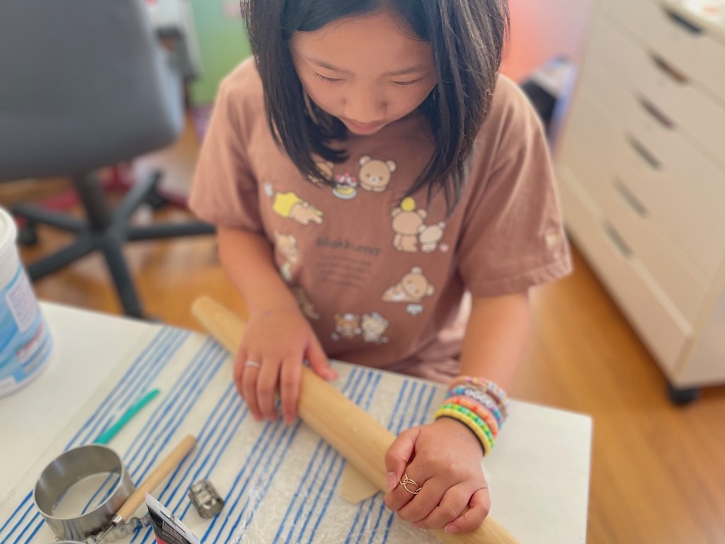 Child rolls out air dry clay between two sheets of plastic wrap.