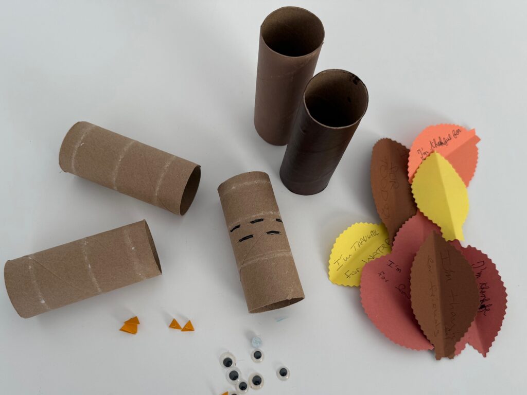 Materials needed for thankful turkeys: toilet paper rolls, construction paper feathers, googly eyes, and cardstock beaks.