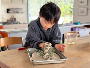 Child makes a volcano from air-dry clay with a spice jar as the base.