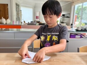 Child folds a paper airplane in preparation for playing the airplane game.