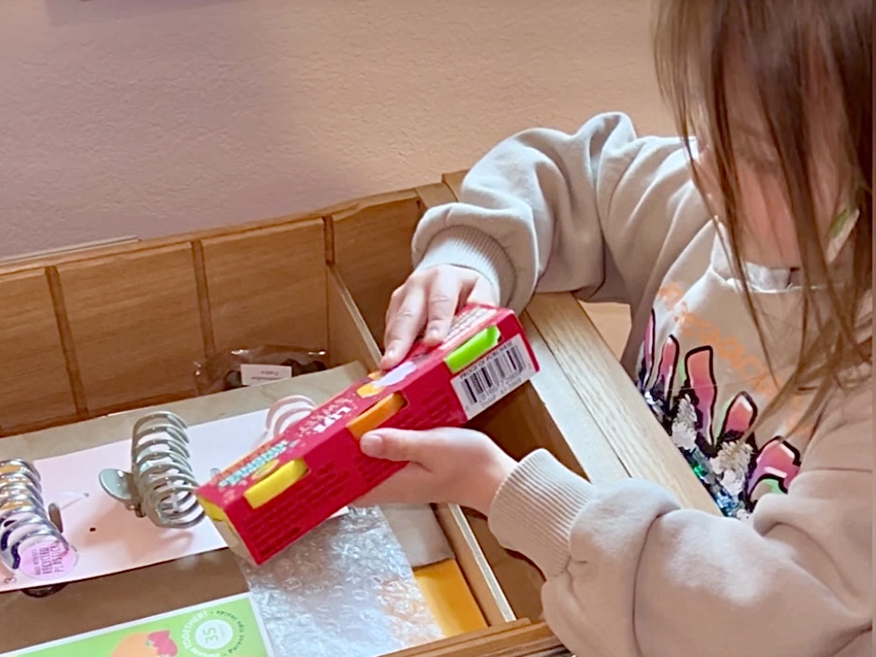 Child finds a surprise, a new packet of Play-Doh, in her desk upon her arrival at her grandparents' home.