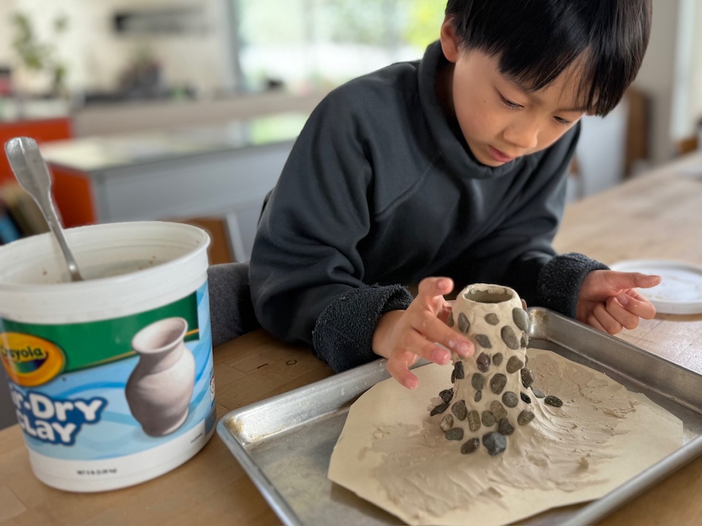 Child builds a volcano out oa air dry clay. He'll create an volcano eruption with baking soda, vinegar, and dish soap.