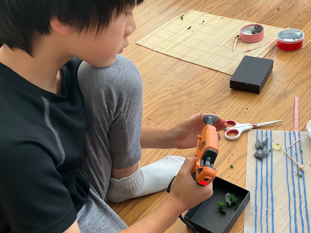 Child glues rocks and moss into the box that will become his zen garden.