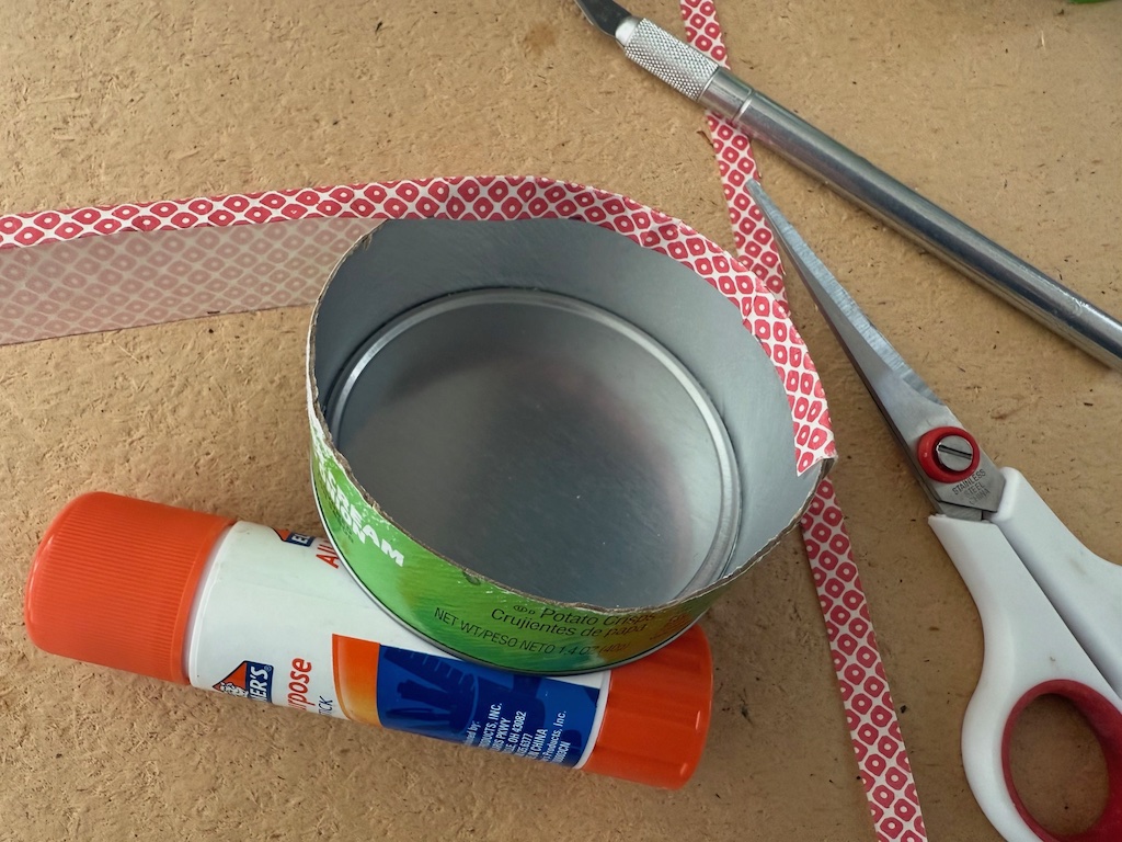 Line the can with a strip of origami paper, folding the top edge over the ragged cut edge of the can.