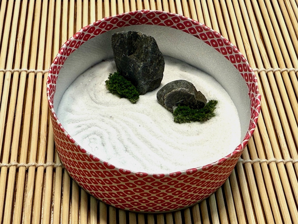 The finished Pringles can zen garden features two rocks with artificial moss on white sand that has been raked into a pattern.