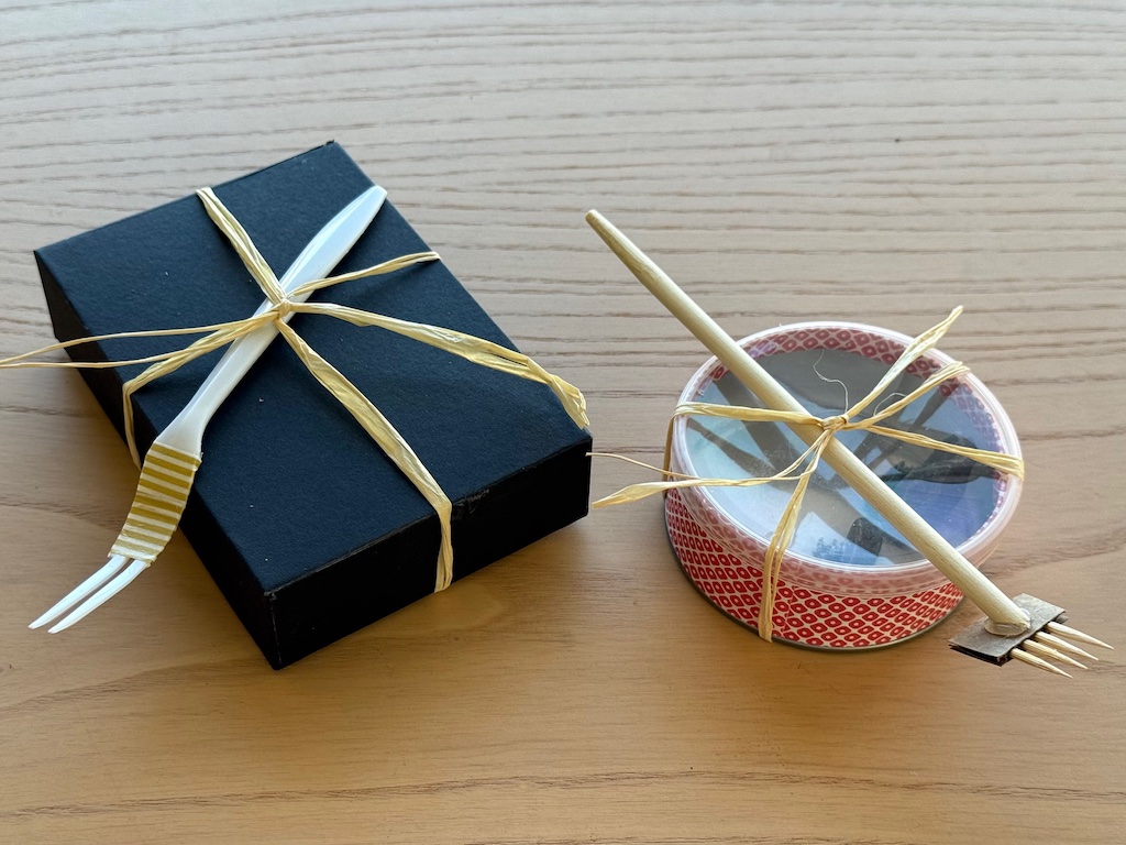 Finishged zen garden present, covered and tied with raffia. The box garden holds a plastic fork; the Pringles can garden holds a toothpick rake.