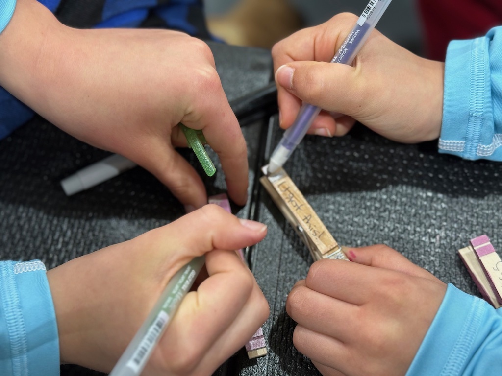 Girls writing messages and decorating clothespins to make clips that they will distribute during the volleyball tournament.