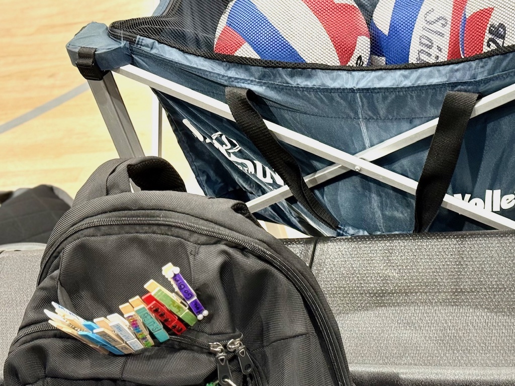 Backpack with clips sits on the bleacher at the volleyball court.