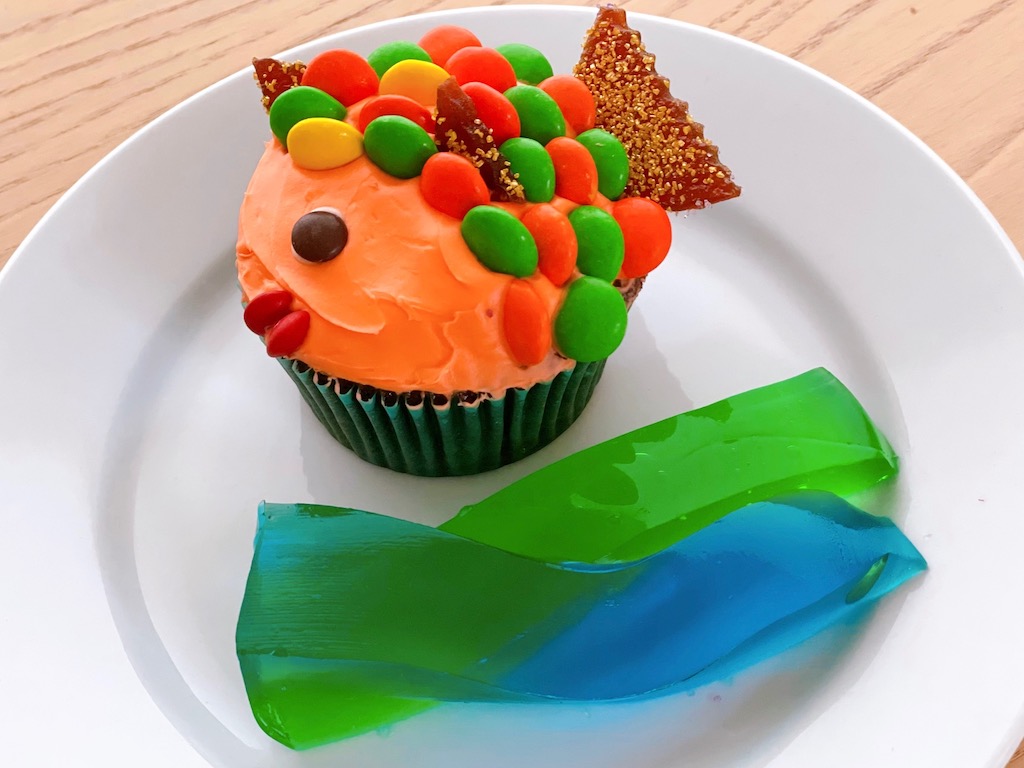 Fish cupcakes use M&Ms for scales and sits next to waves of colored gelatin strips. 