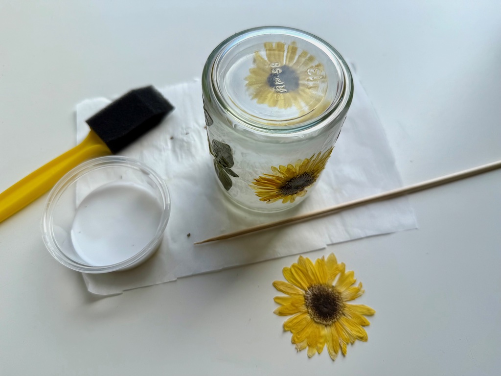 Sponge brush, white school glue, and pressed flowers are used to make.a decorative jar.