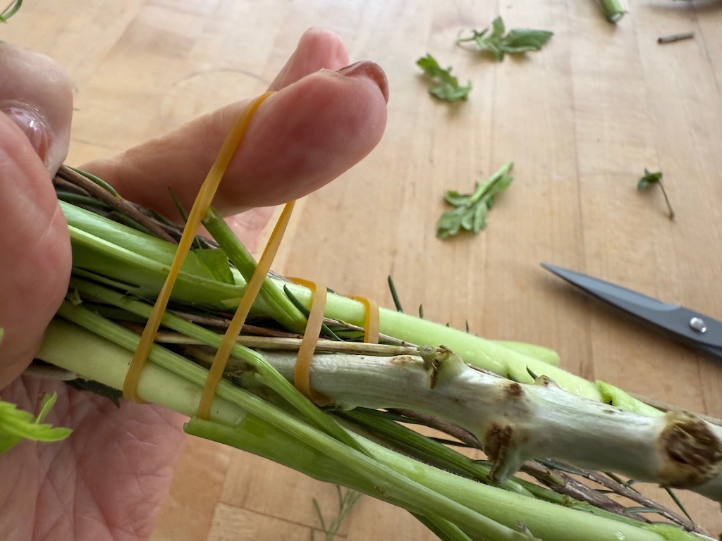 To rubber band flowers, hook the rubber band on the hardiest stem and wrap the rubber band around the bunch of flowers, catching the  end of the rubber band back under the stem.