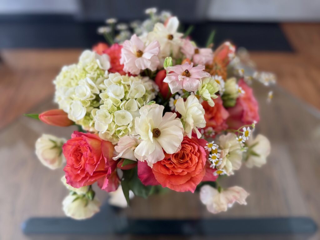 Flower bouquet is seen from the top. It features a multitude of flowers in coral and white.