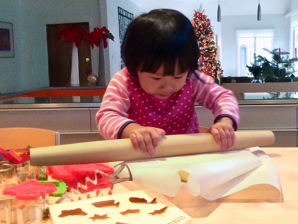 Child rolling out cookie dough to make Christmas cookies.