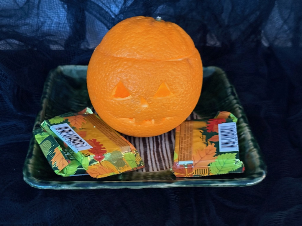 Jack-o-lantern carved from an orange is lit with a battery-operated tea light.