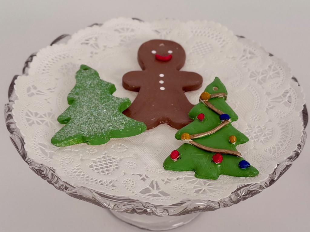Samples of air dry cookies: Christmas tree with glitter, gingerbread man, and Christmas tree with tinsel and ornaments made from air dry clay.