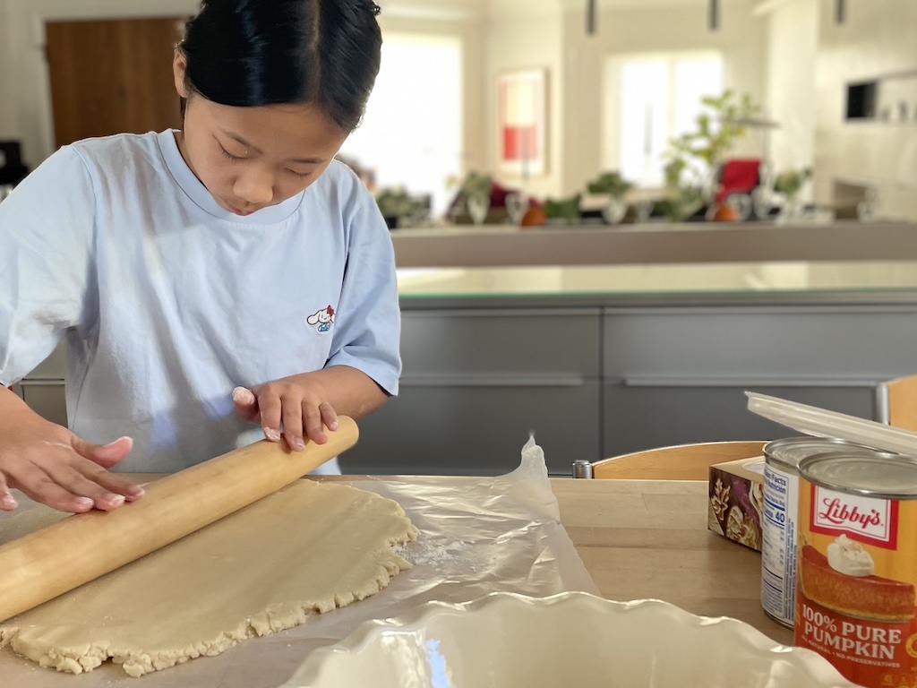 Child rolls out crust or pumpkin pie.
