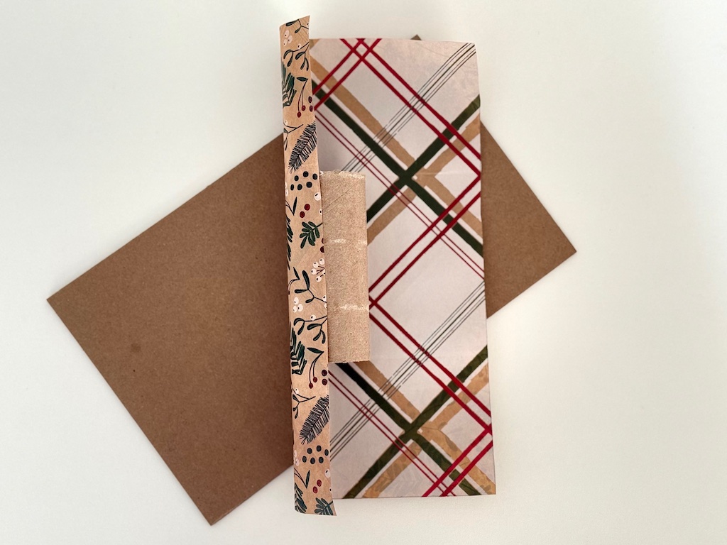 Toilet paper roll is lined up on gift wrap paper, ready to roll.