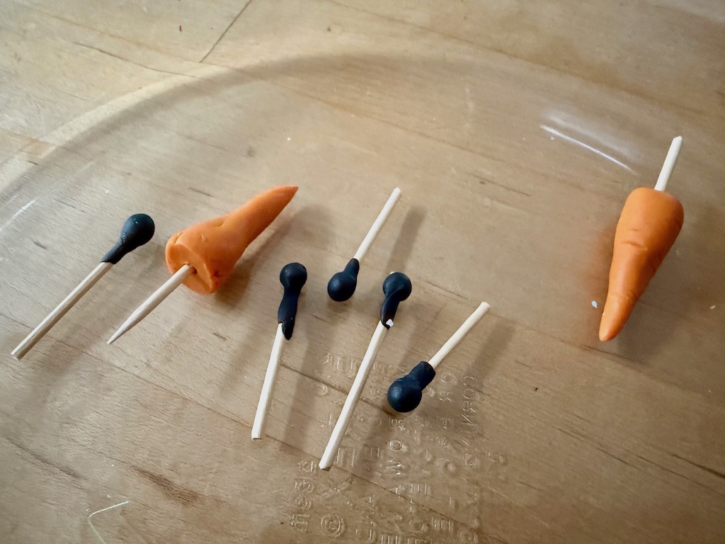 Eyes, buttons, and carrot noses are made from polymer clay with small lengths of skewer attached. After baking to harden, the skewers can be inserted into the snowman to hold features in place.