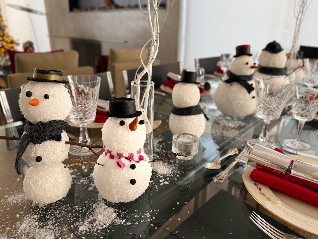 Dinner table is set with snowmen as the centerpiece. Artificial snow and birch branches with fairy lights complete the setting.