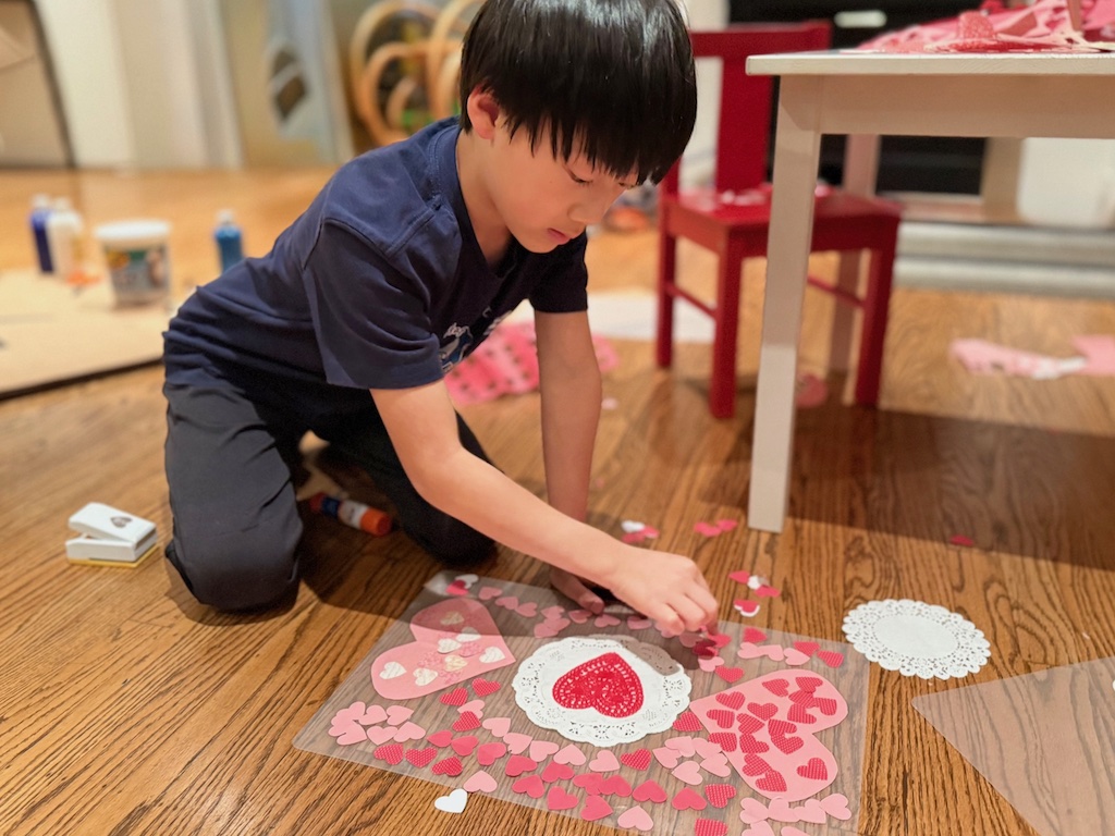 Child glues down paper hearts onto clear plastic placemat.