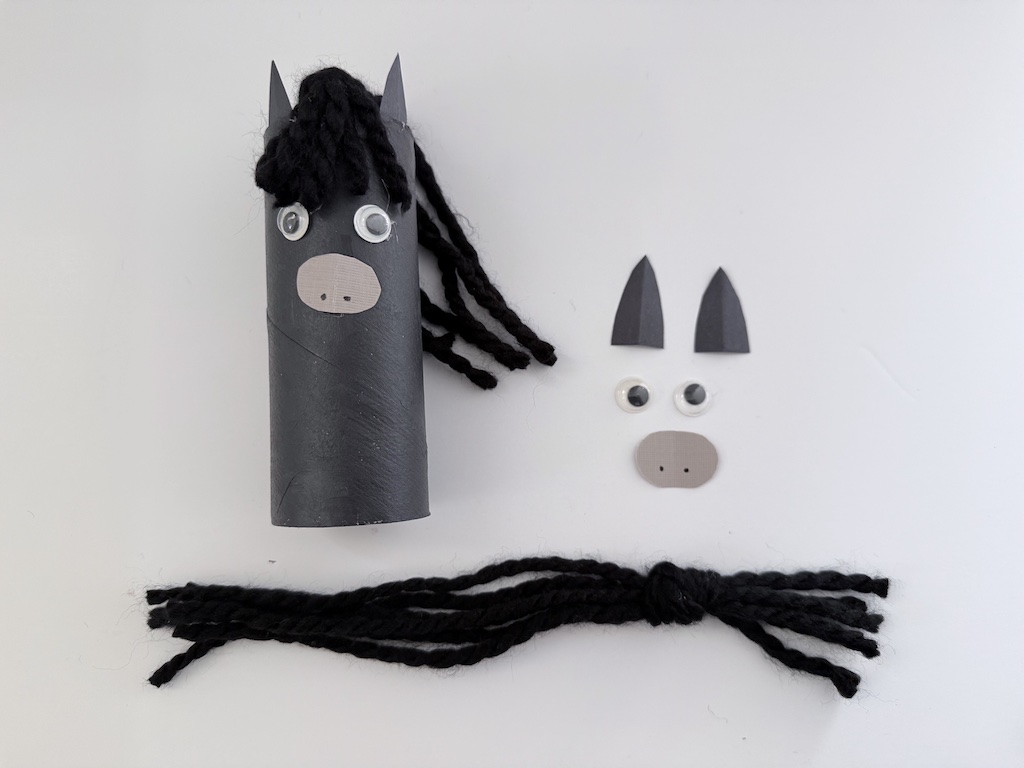 Elements of a Chinese New Year horse: toilet paper roll, construction paper ears and muzzle, googly eyes, and yarn scraps.