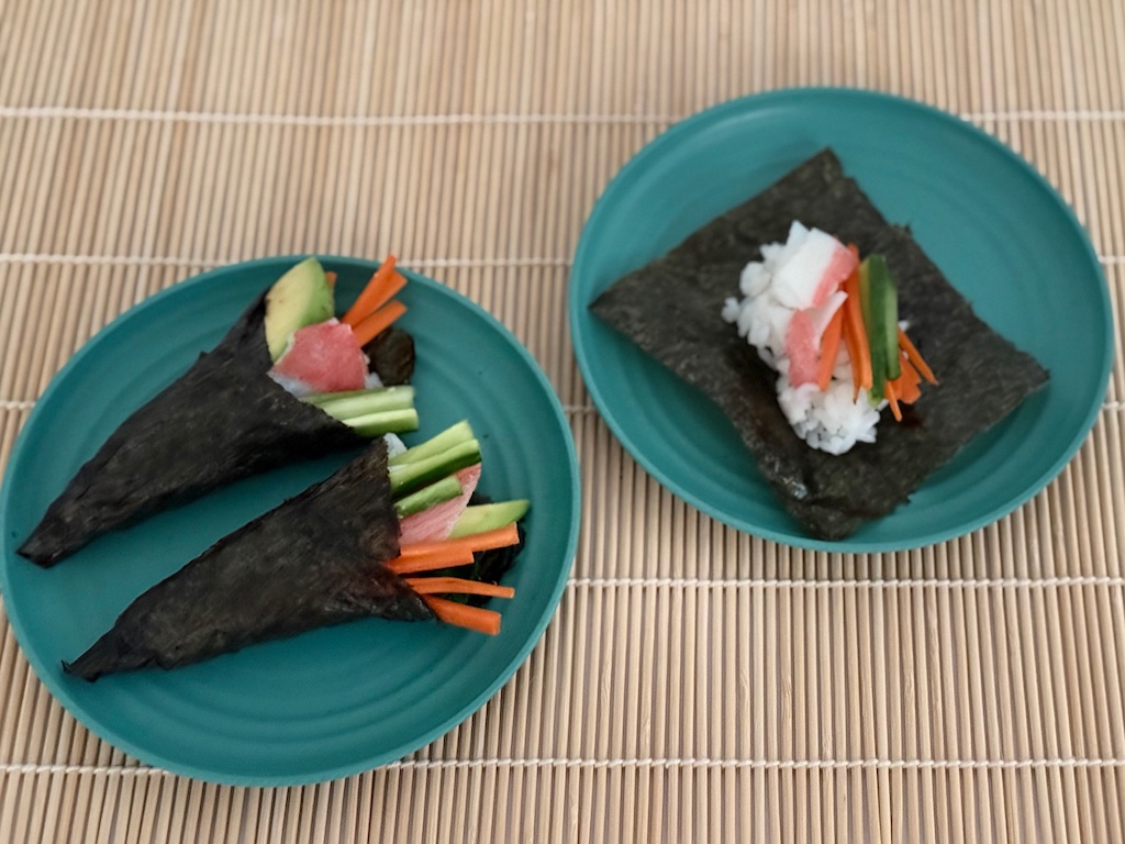 Temaki, hand-rolled sushi, is made by adding seasoned rice to nori squares, along with vegetables and imitation crab. Wrap the nori to encase the ingredients.