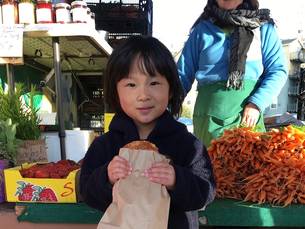 Child eats a pastry at the farmers market. A trip to a farmers market is a fun excursion for some children.