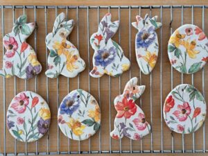 Air dry clay, cut with Easter cookie cutters and overlaid with a flowered paper napkin, sits on a rack to dry.