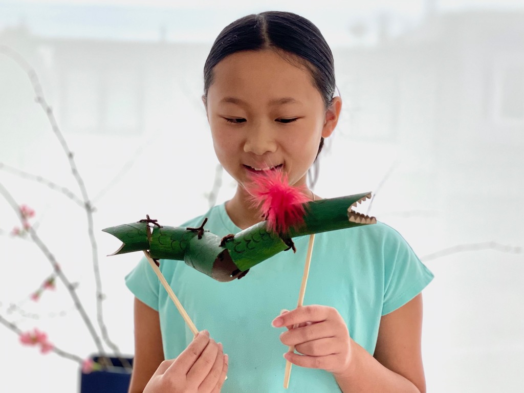 Child plays with dragon made from recycled toilet rolls and chopsticks.