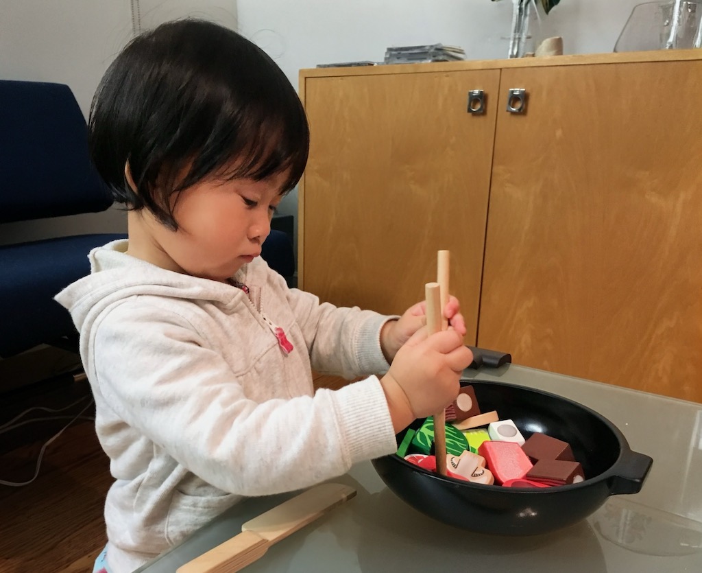 Child pretends to cook with toy chopsticks.
