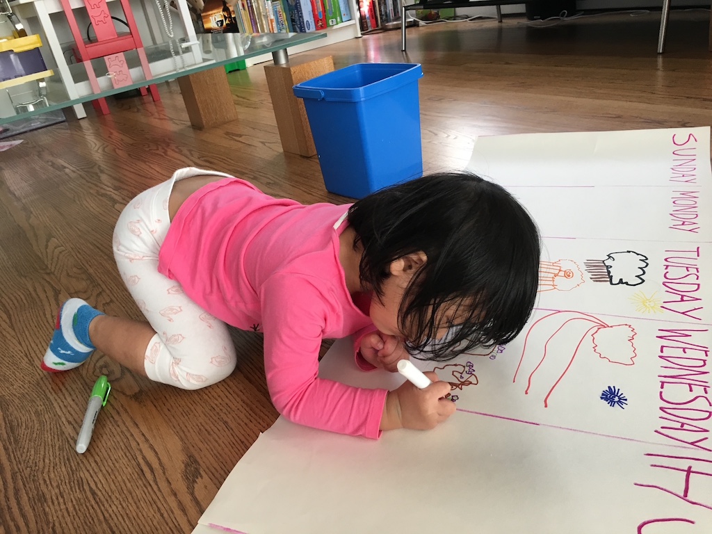Child drawing on a large sheet of paper marked with the days of the week. She is to draw what she saw on her walk home from preschool, every day.