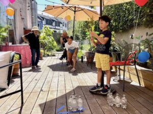 Grandchild tries to knock water bottle pins over during annual summer party.