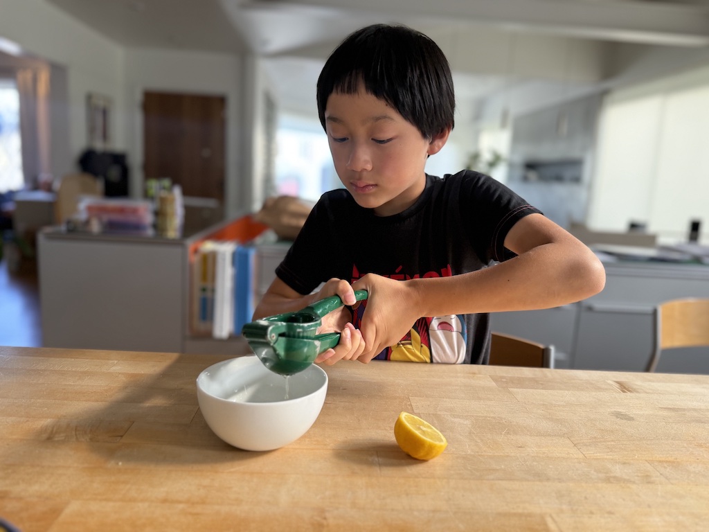 Child squeezes lemon juice into a bowl. He'll use a q-tip dipped in the lemon juice to write his message.