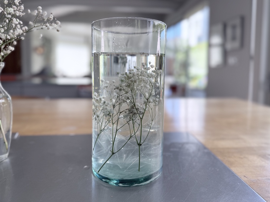Baby's breath is submerged in a tall glass vase. It is held in place with crumpled clear plastic sheet protectors.