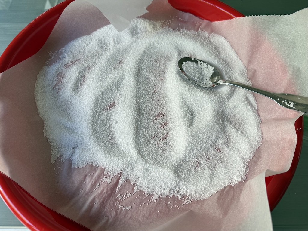 Wet candle sand, extracted from flower arrangements, is dried in a tray lined with parchment paper to be reused again.