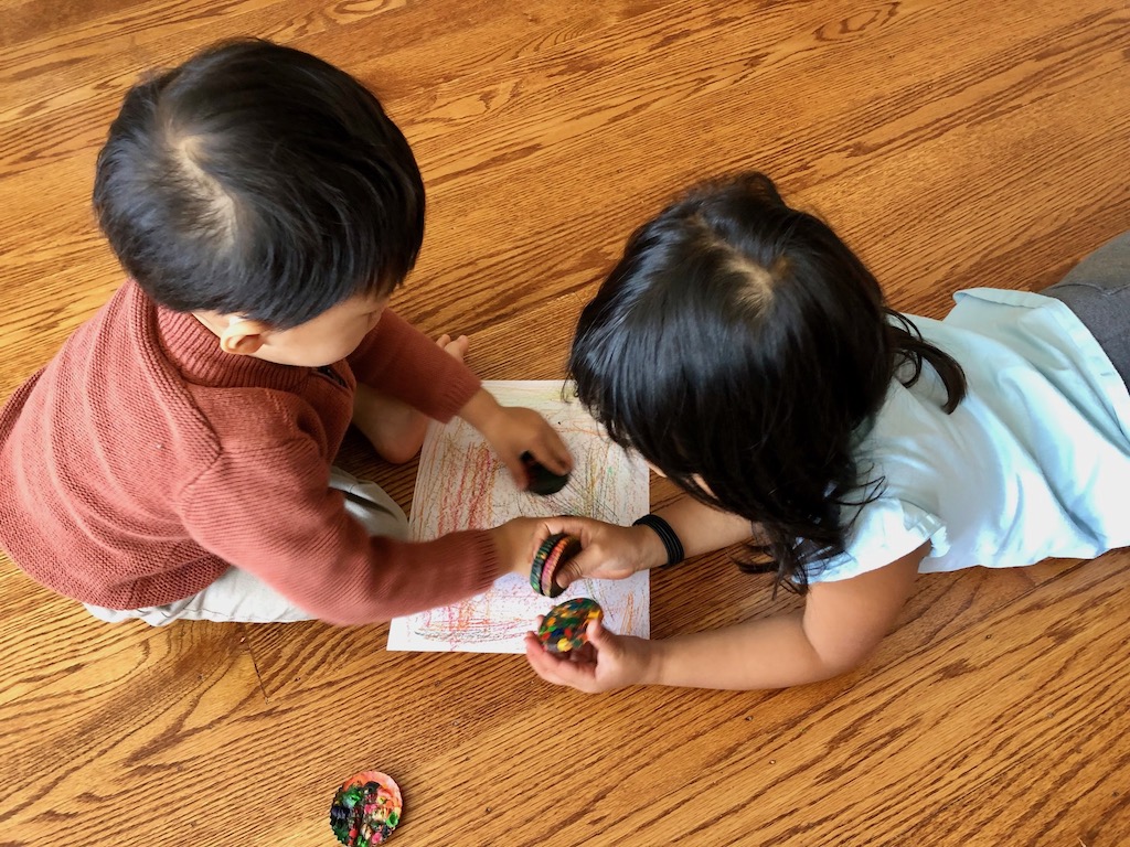Children lying on the floor, coloring with multicolor crayon disks made by melting broken crayons to form new crayons.