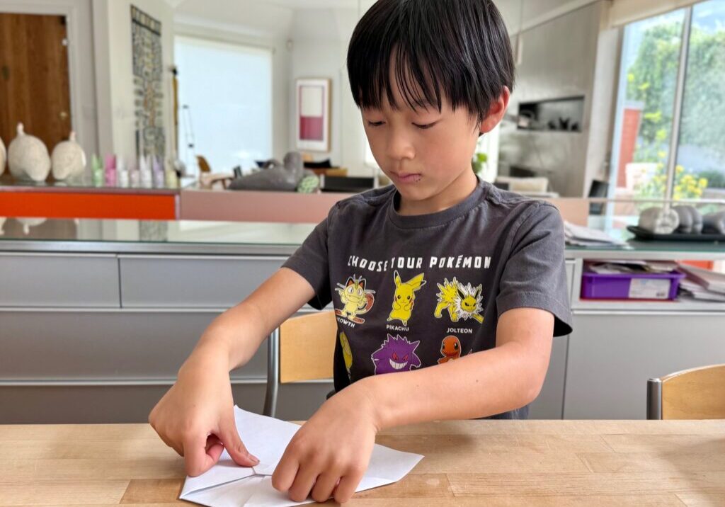 Child folds a paper airplane in preparation for playing the airplane game.