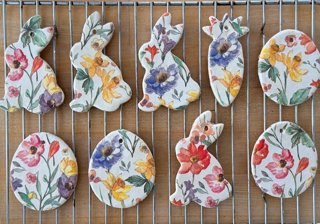 Air dry clay, cut with Easter cookie cutters and overlaid with a flowered paper napkin, sits on a rack to dry.