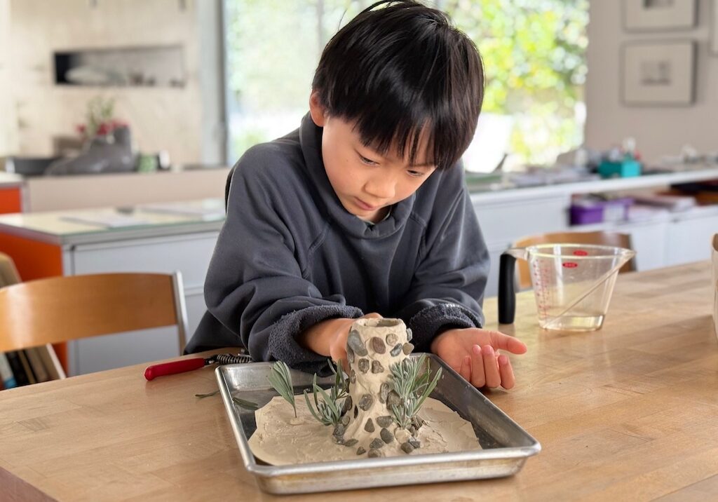 Child makes a volcano from air-dry clay with a spice jar as the base.